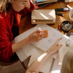 Dois estudantes estudam à mesa, cercados por livros, anotações e materiais escolares.