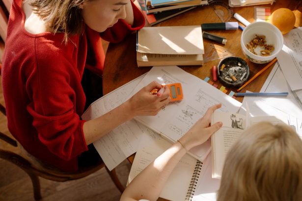 Dois estudantes estudam à mesa, cercados por livros, anotações e materiais escolares.