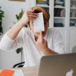 Empresária mostra um recibo em um ambiente de trabalho doméstico, com computador e documentos ao redor.