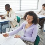 Grupo diverso de estudantes realiza uma prova em uma sala de aula iluminada.