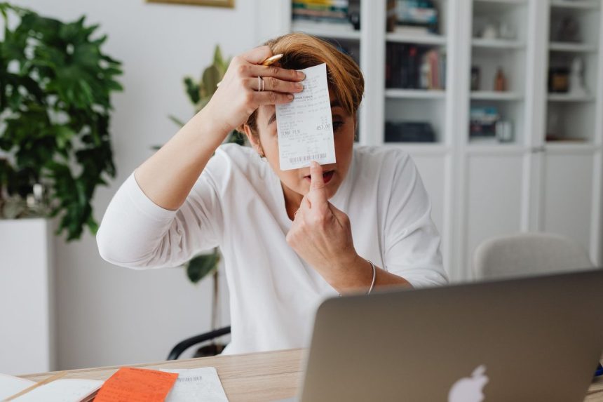 Empresária mostra um recibo em um ambiente de trabalho doméstico, com computador e documentos ao redor.